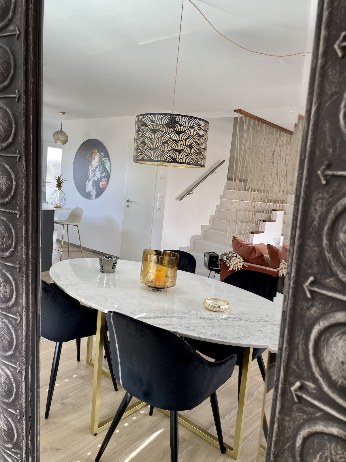 reflet dans le miroir à cadre métalique gris d'une table repas en marbre blanc avec fauteuils en velours noir, escalier au fond